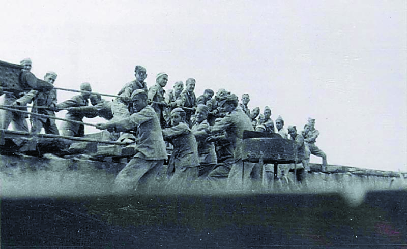 Un grupo de prisioneros tira de grandes sogas a mano para mover por railes de tren un gran cañón traído hasta el puerto de Tarifa en barco y que había que llevar a unas de las baterías de artillería de costa de este municipio.