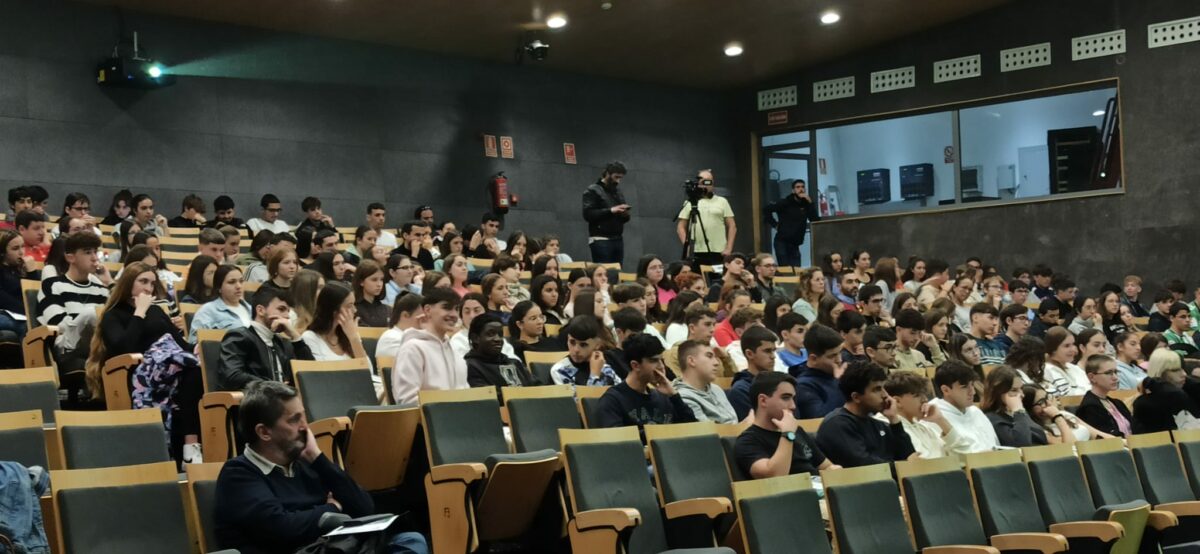Alumnos y alumnas escuchan la conferencia de Ángel del Río en el salón Levante del palacio.